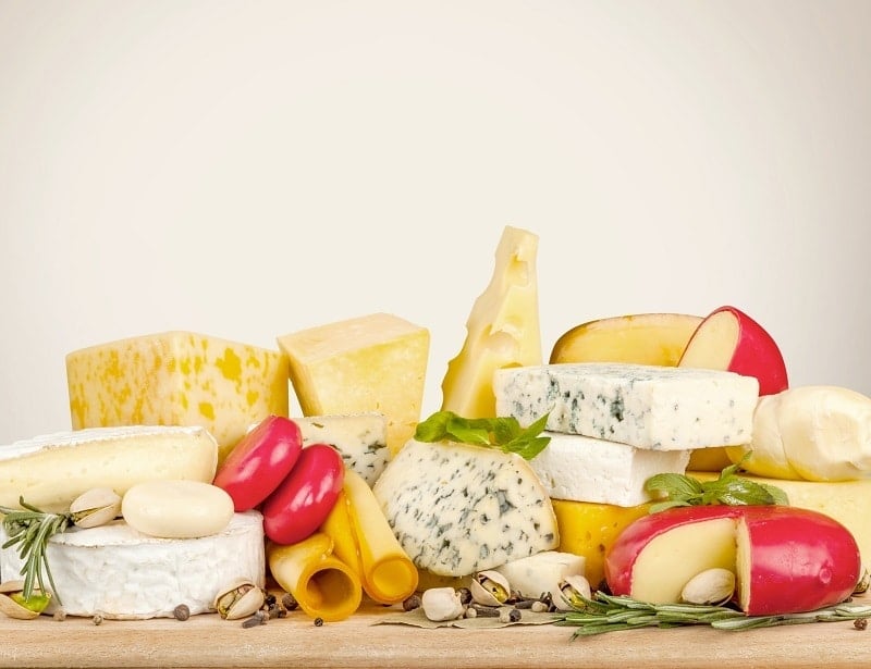 several different types of cheese on a wood table on a white background