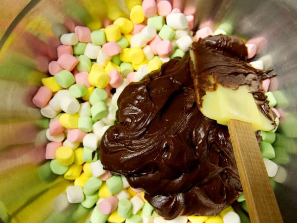 a spatula folding the chocolate mixture into a bowl of colored marshmallows