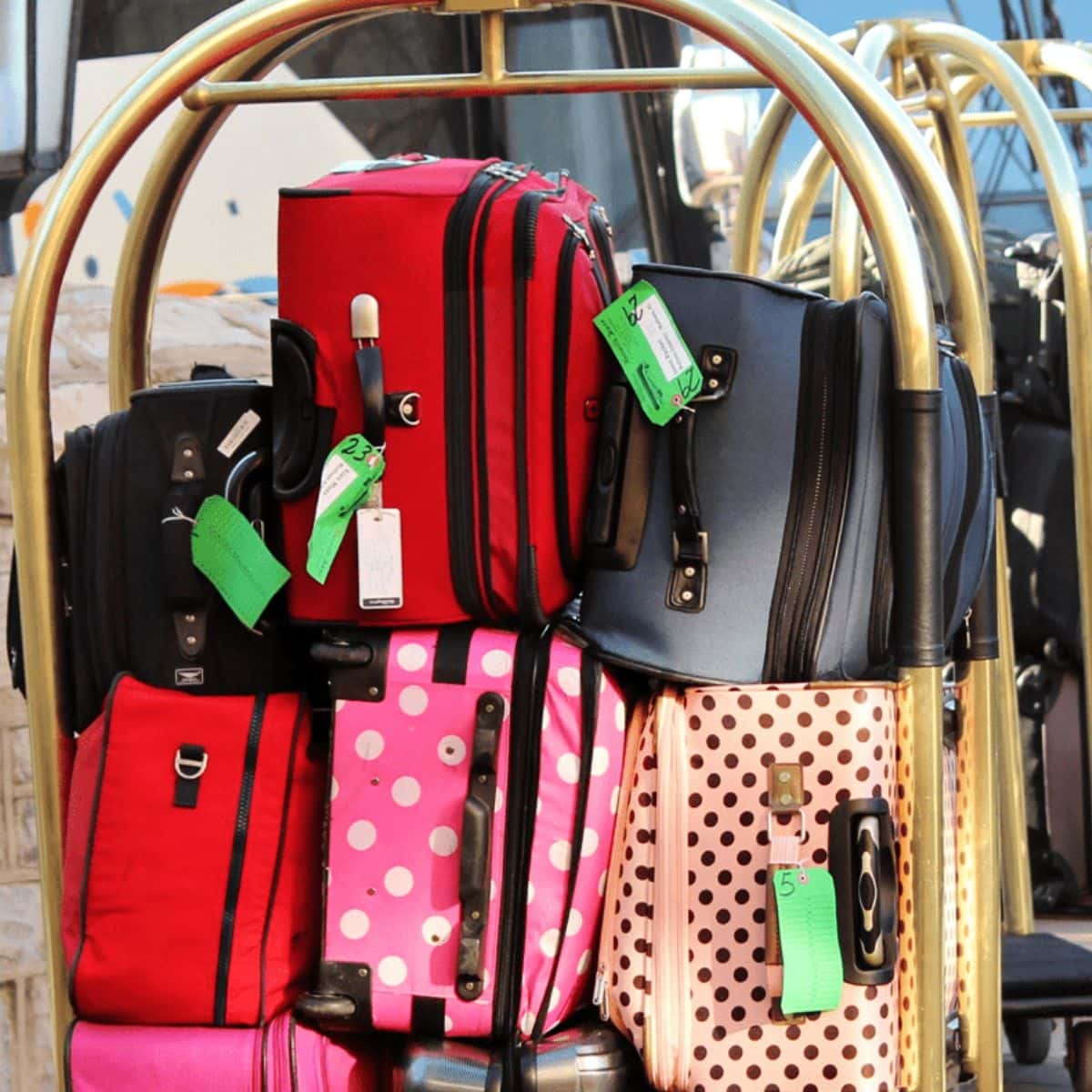 A hotel luggage cart loaded with several suitcases, including red, black, and pink polka-dotted bags with green tags attached—perfect for family travel.