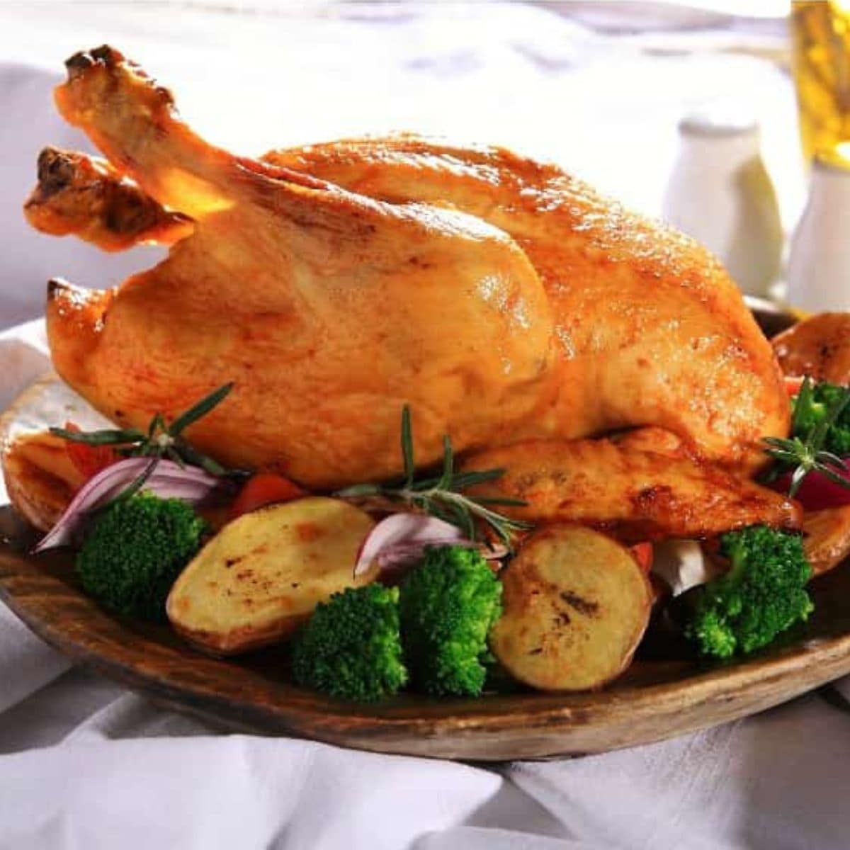 Whole roasted chicken served on a wooden platter with roasted potatoes, broccoli, red onion, and sprigs of rosemary—perfect inspiration for new ways to use rotisserie chicken at home.