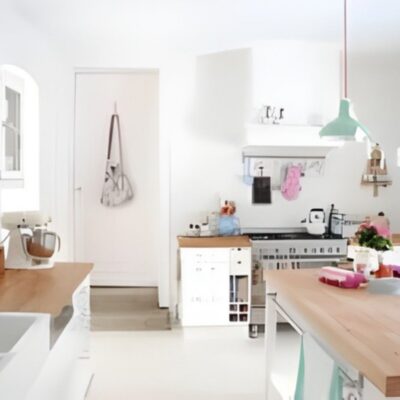 A bright, modern kitchen with wooden countertops, white cabinets, hanging utensils, and a mint green pendant light over a central island—perfectly organized for easy spring cleaning.