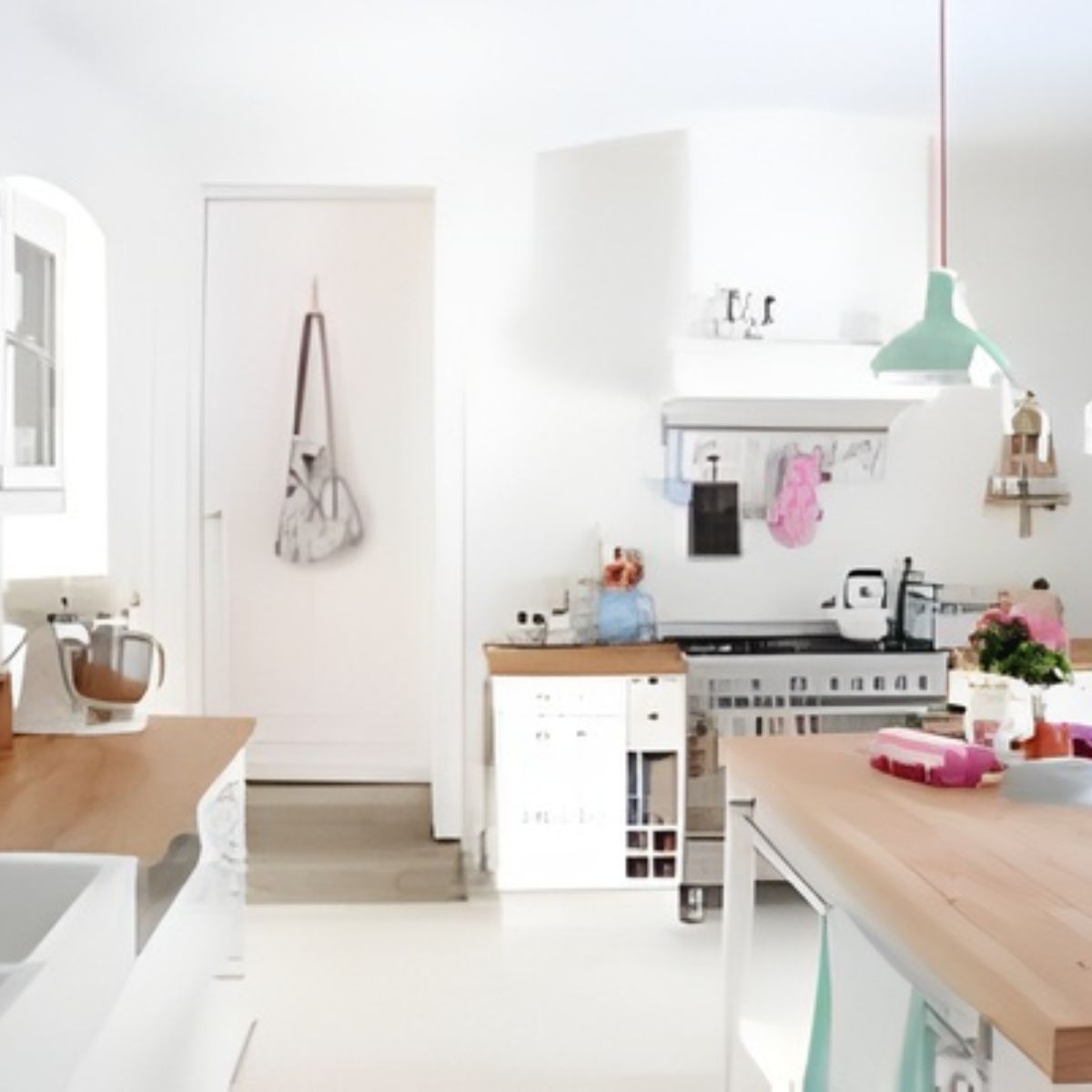 A bright, modern kitchen with wooden countertops, white cabinets, hanging utensils, and a mint green pendant light over a central island—perfectly organized for easy spring cleaning.