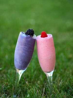 2 Smoothies in the grass outside. One pink and one purple