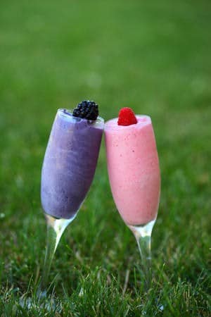 a purple and pink smoothie in two glasses topped with berries in the grass