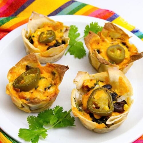 Four chicken enchilada cups topped with melted cheese and jalapeño slices are served on a white plate, garnished with fresh cilantro.