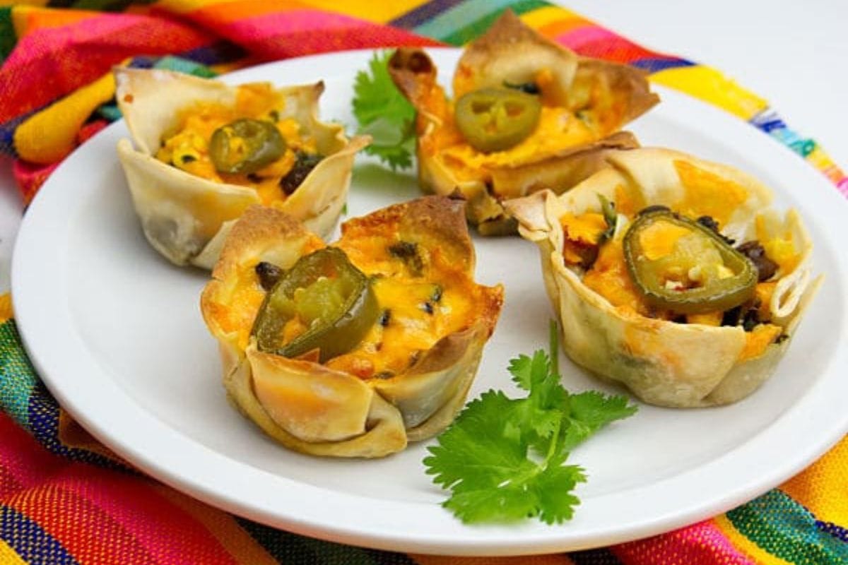 Four chicken enchilada cups topped with jalapeño slices are arranged on a white plate with cilantro garnish.