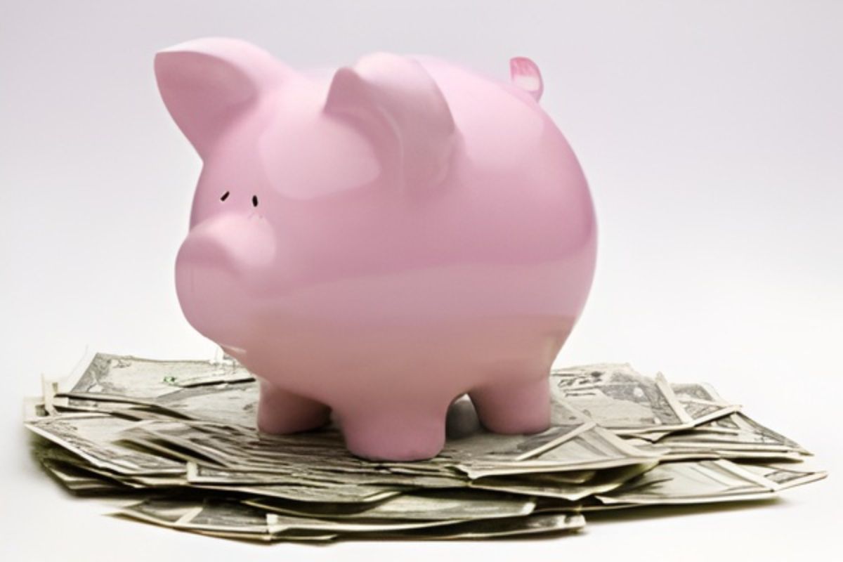 Pink Piggy Bank On Top Of A Pile Of One Dollar Bills A pink piggy bank sits on top of a pile of scattered US dollar bills against a plain white background.