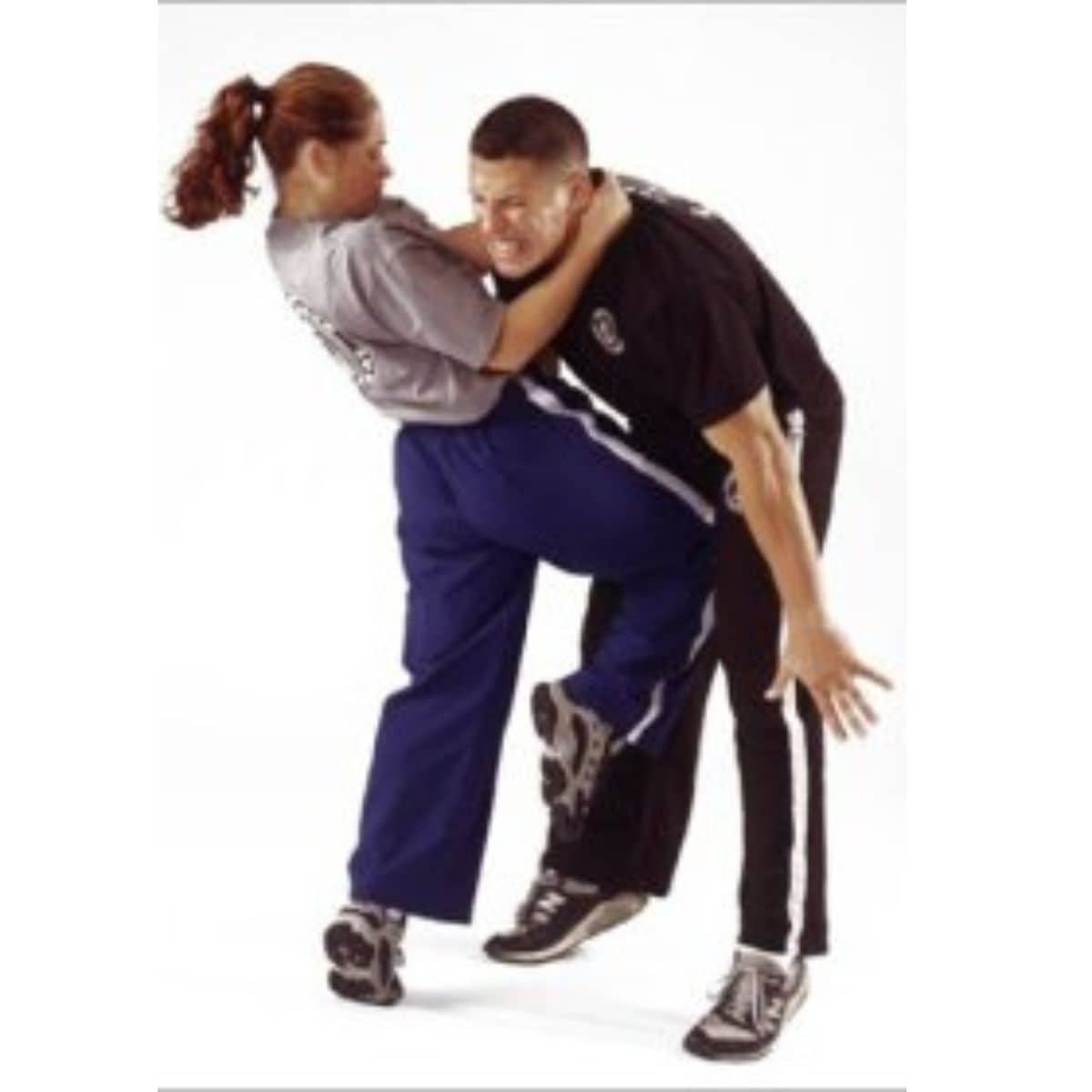 A woman in athletic clothing demonstrates self defense tips for women by kneeing a man in the groin while holding his shoulders.