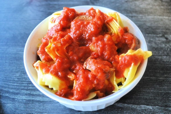 a white bowl filled with sausage and tortellini and topped with marinara sauce
