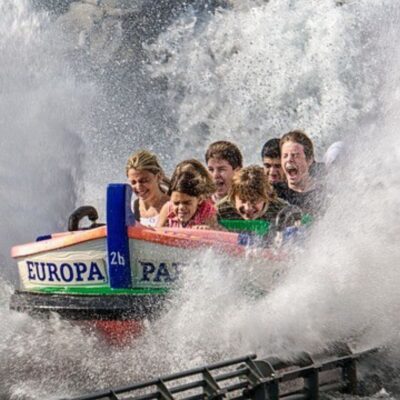 Six people on a Europa Park water ride, getting splashed by a large wave, their faces lit with excitement and surprise—a perfect moment of amusement park family fun.