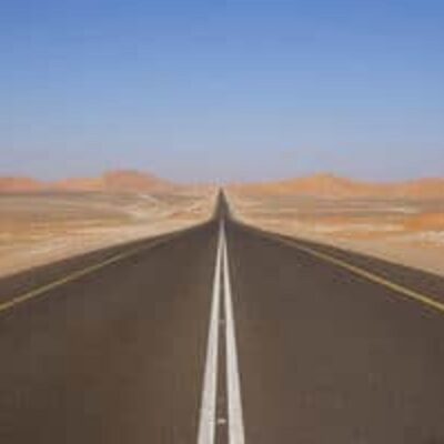 A straight, empty road stretches into the distance through a barren desert landscape under a clear blue sky—perfect scenery for starting your next adventure with a thorough road trip checklist.
