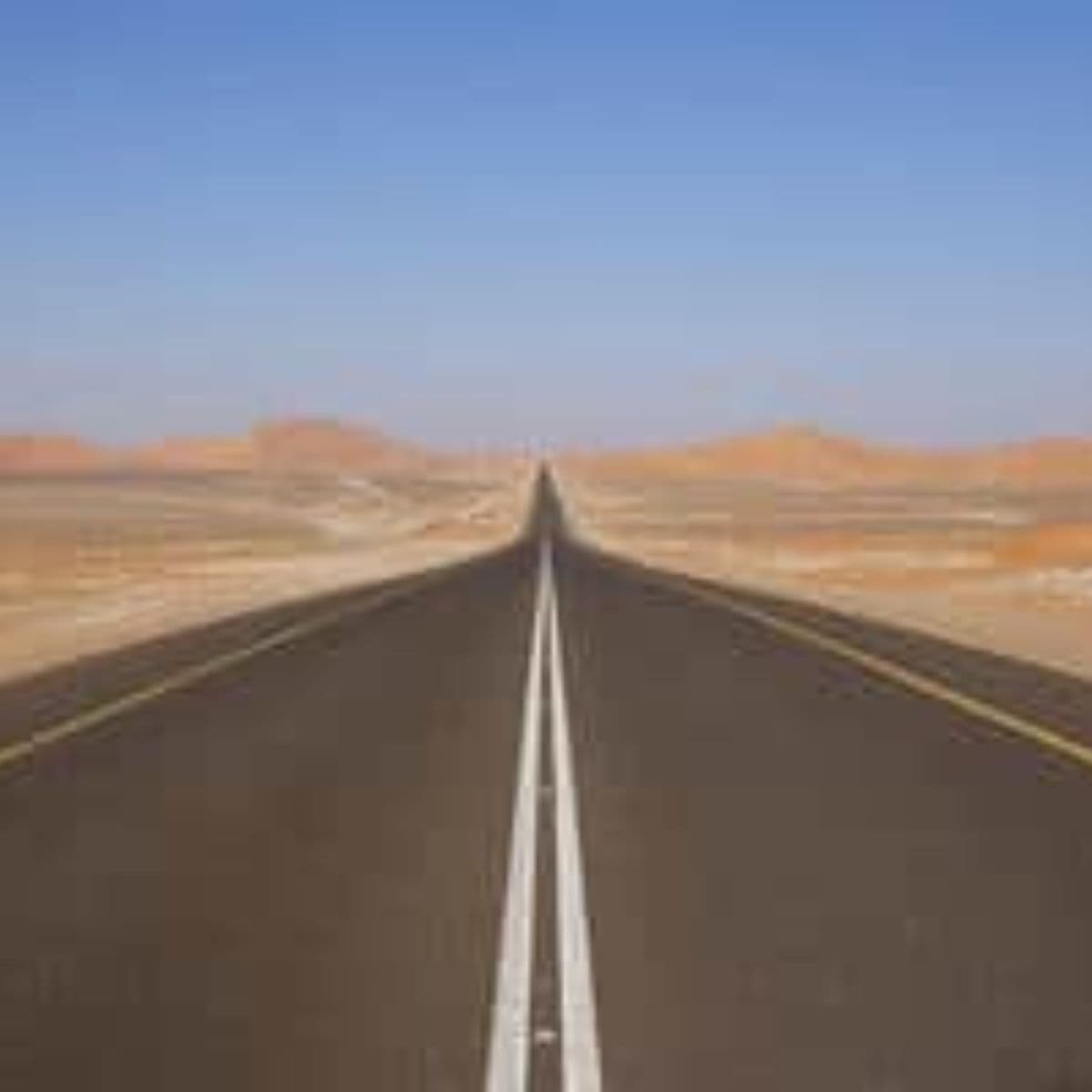 A straight, empty road stretches into the distance through a barren desert landscape under a clear blue sky—perfect scenery for starting your next adventure with a thorough road trip checklist.