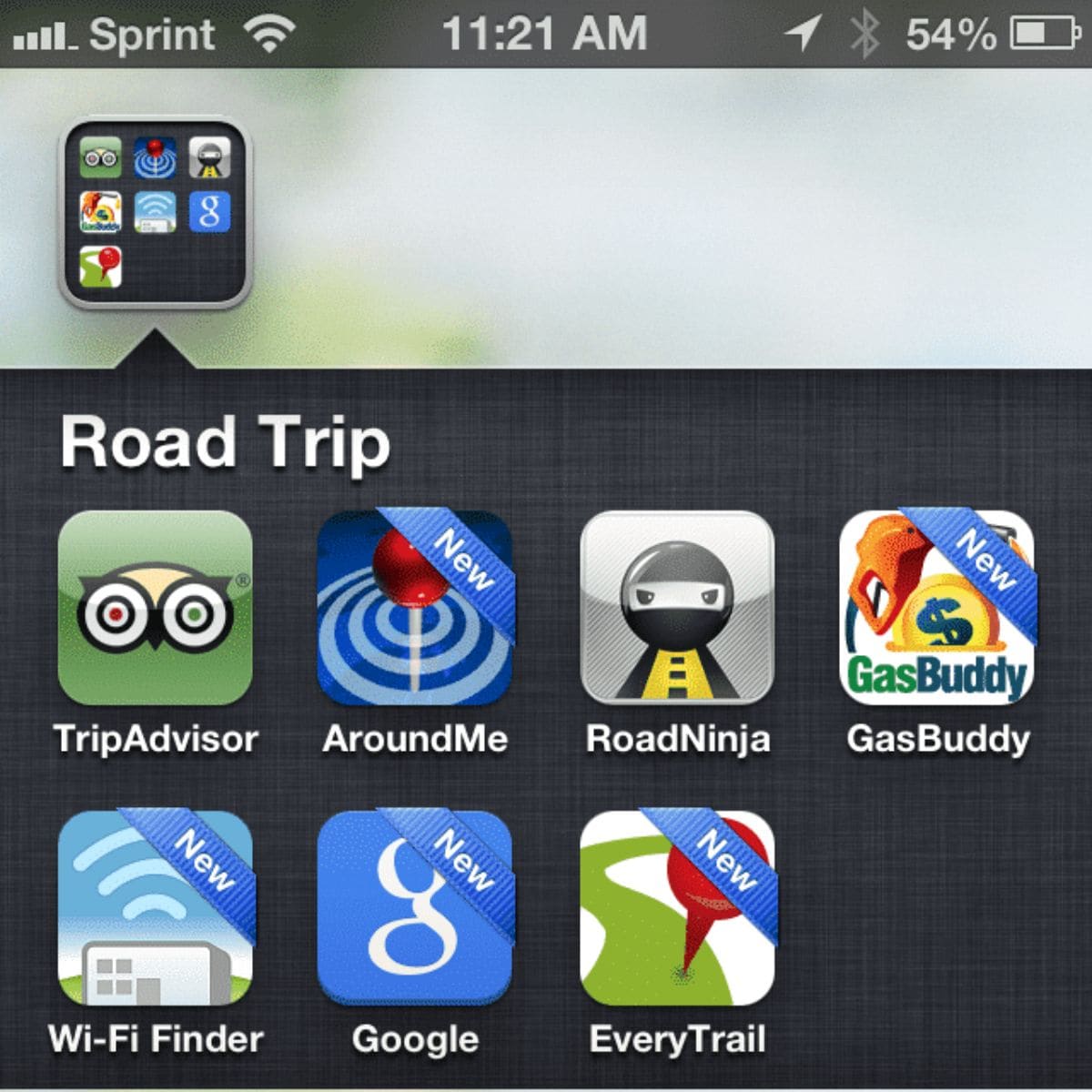 Screenshot of a smartphone screen showing a "Road Trip" folder containing seven travel-related app icons, highlighting some of the best apps for road trips like TripAdvisor, AroundMe, RoadNinja, GasBuddy, Wi-Fi Finder, Google, and EveryTrail.