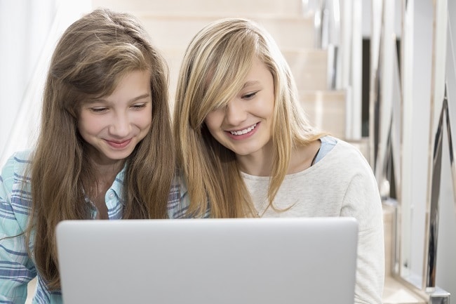 two teen girls sitting on a staircase looking at a laptop