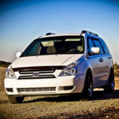 A white minivan is parked on a gravel surface outdoors under a clear blue sky—a reminder to keep your car running smoothly for every journey.