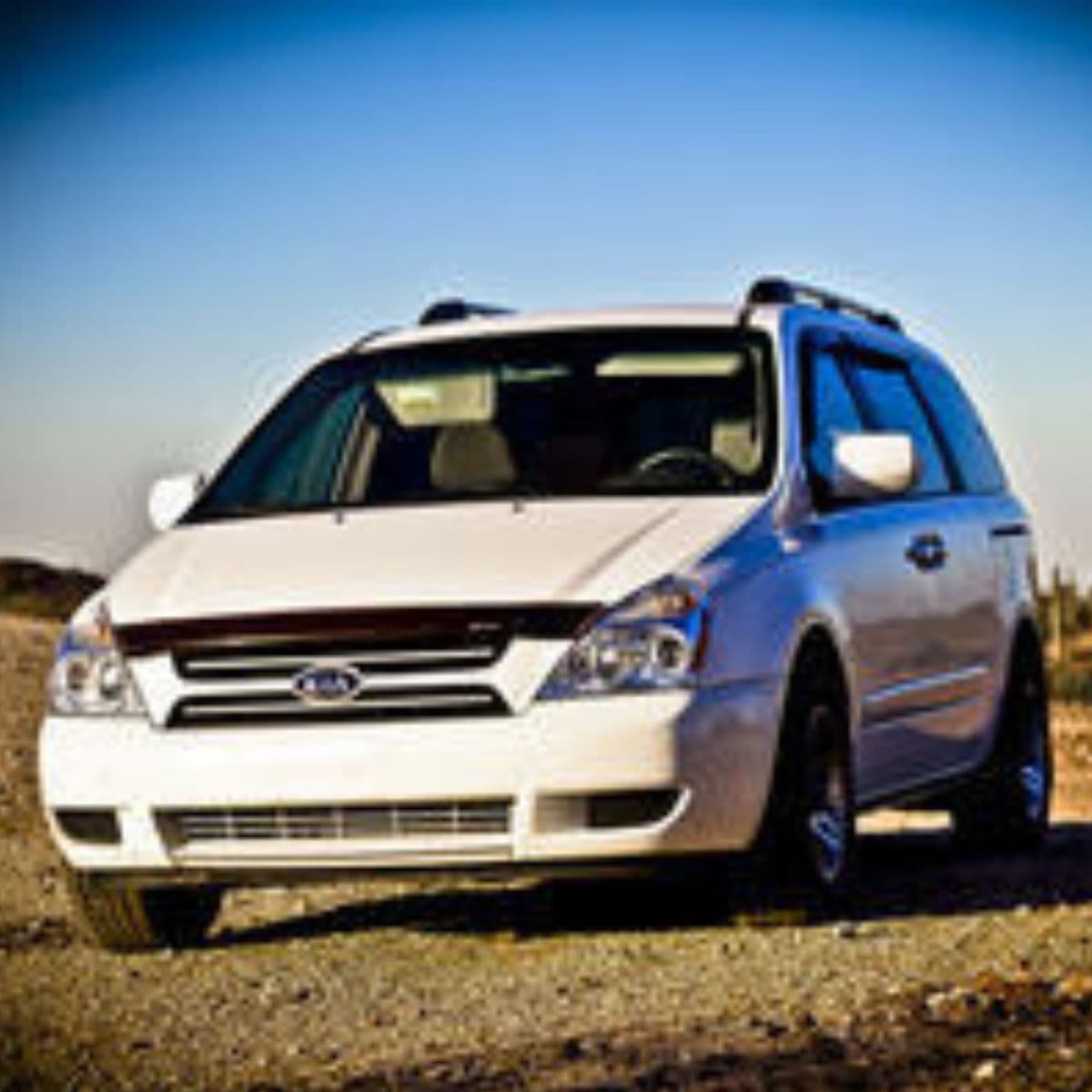 A white minivan is parked on a gravel surface outdoors under a clear blue sky—a reminder to keep your car running smoothly for every journey.
