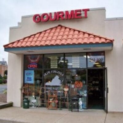 A storefront with a red "GOURMET" sign above the entrance and large glass windows displaying various items. The door is open, an "OPEN" sign is visible—one of many reasons to shop mom and pop for a welcoming, authentic experience.