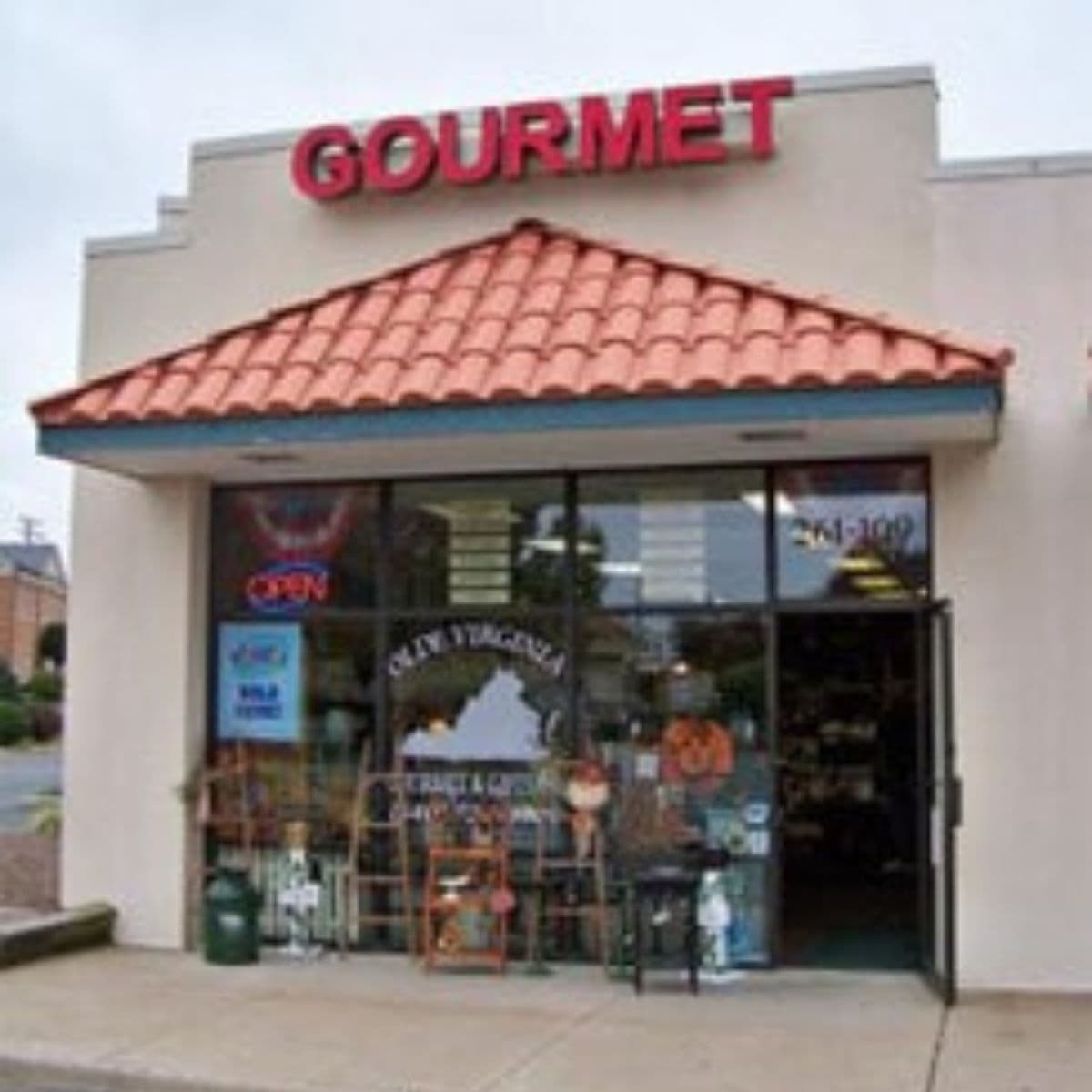 A storefront with a red "GOURMET" sign above the entrance and large glass windows displaying various items. The door is open, an "OPEN" sign is visible—one of many reasons to shop mom and pop for a welcoming, authentic experience.