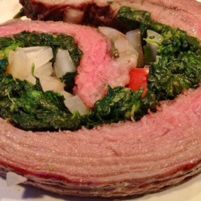 Close-up of a spinach stuffed flank steak rolled and filled with chopped onions and red bell peppers.