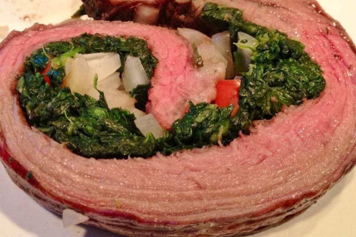 Close-up of a spinach stuffed flank steak roulade, sliced to reveal a savory filling.