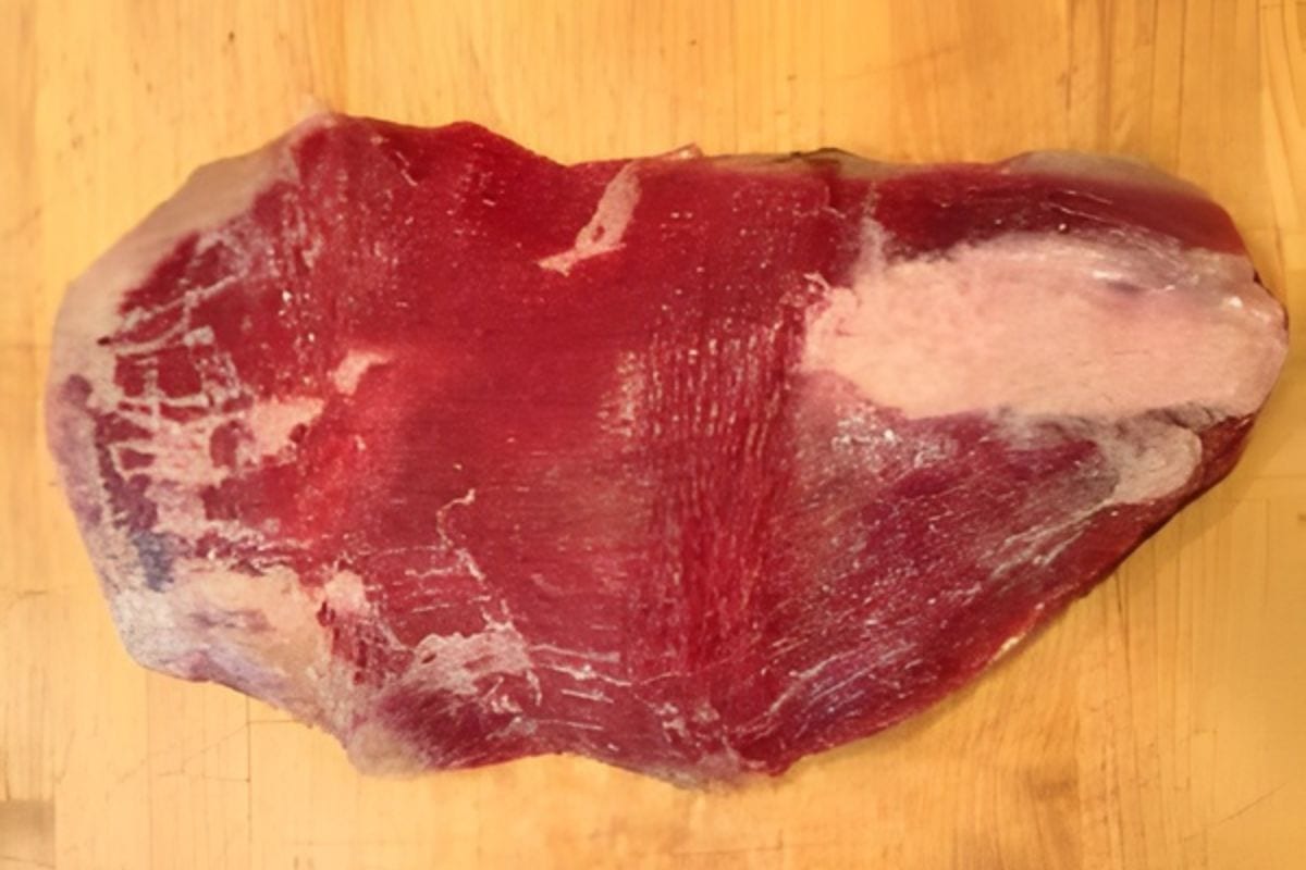 A raw piece of red meat, perfect for making spinach stuffed flank steak, with some fat and connective tissue.