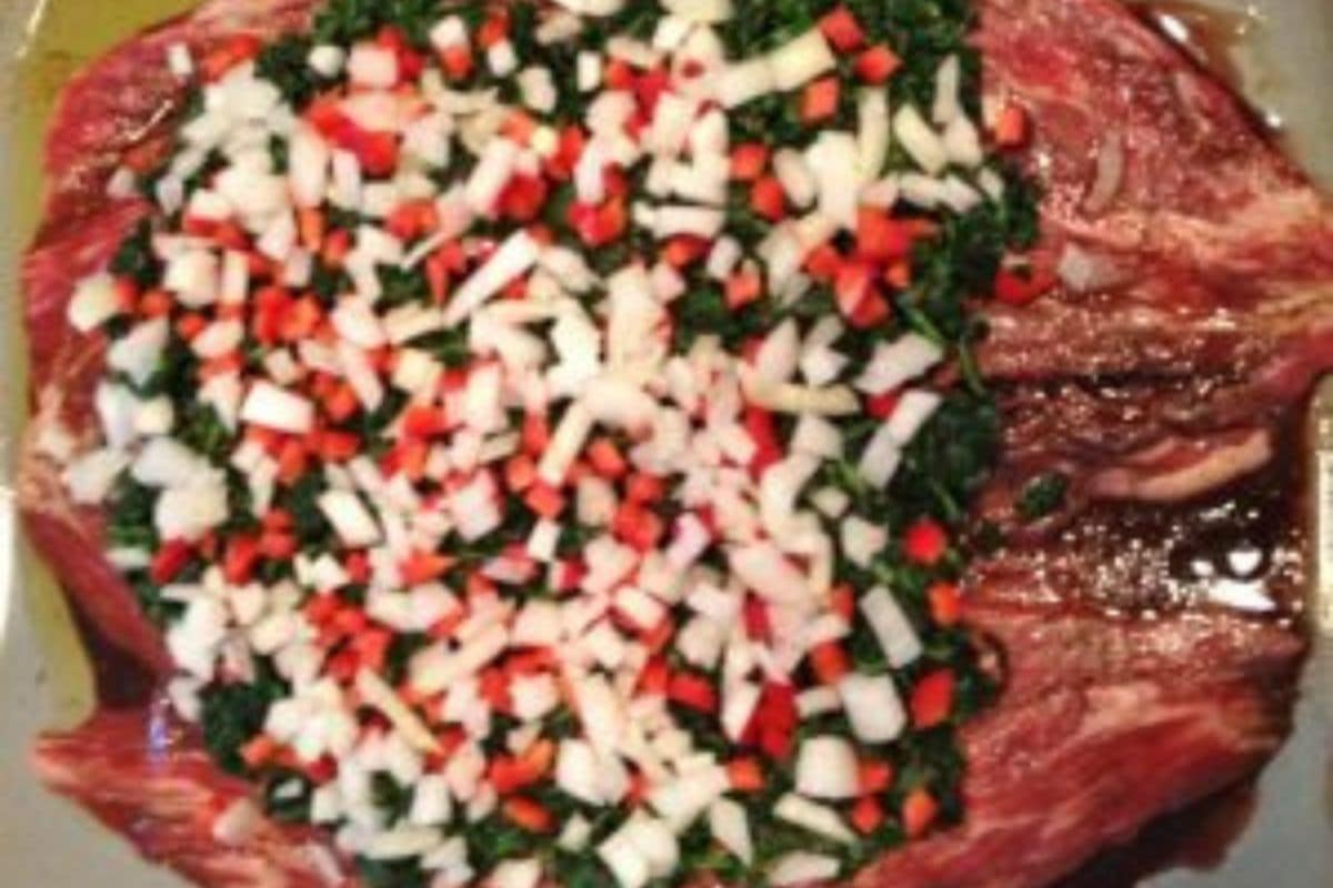 Raw beef topped with a mixture of chopped onions, red bell peppers, and leafy greens, prepared on a tray.