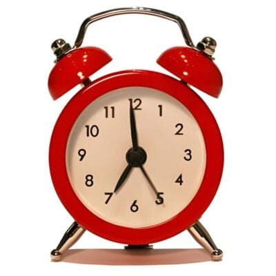 A red analog alarm clock showing the time as 7:00, with two bells on top and metal legs, against a white background—perfect for timing your next 10 minute workout.