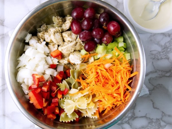 chicken, vegetables, grapes and pasta in a metal bowl on a gray kitchen counter