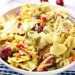 A bowl of chicken pasta salad featuring multicolored bowtie pasta, grapes, diced celery, carrots, and bell peppers coated in a creamy dressing.