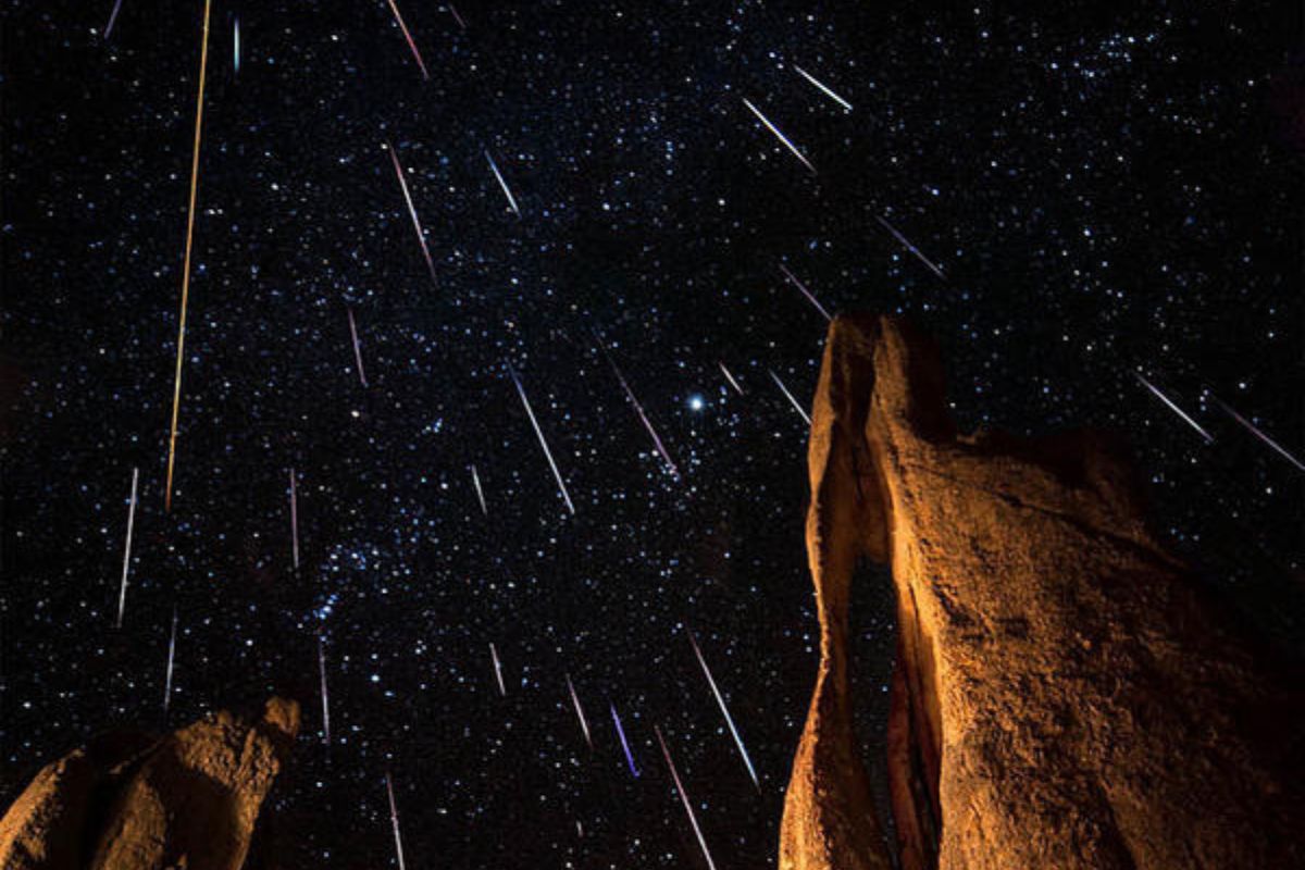 Rocks in the foreground with a clear night sky above, showcasing a dazzling meteor shower as numerous meteor streaks light up the night.