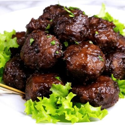 A plate of savory glazed meatballs garnished with chopped herbs, served on a bed of fresh green lettuce.