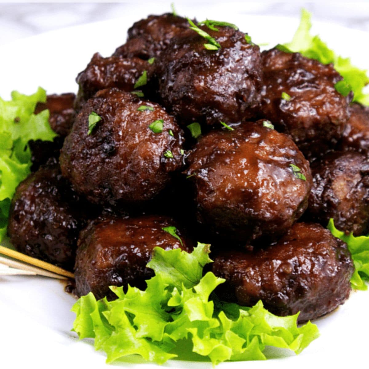 A plate of savory glazed meatballs garnished with chopped herbs, served on a bed of fresh green lettuce.