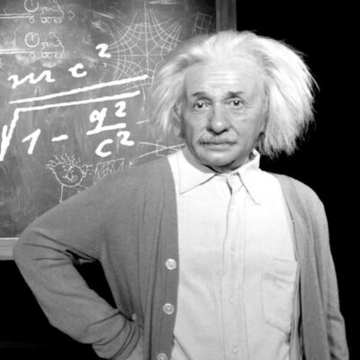 A man with white, wild hair stands in front of a chalkboard filled with mathematical equations and diagrams—just the scene to convince your kids you're a genius.