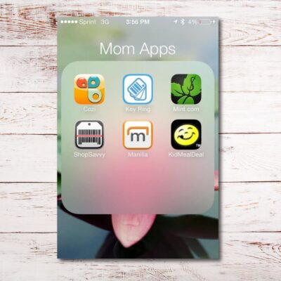 Screenshot of a smartphone folder labeled "Mom Apps" featuring six essential apps for busy moms: Cozi, Key Ring, Mint, ShopSavvy, Manilla, and KidMealDeal.