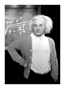 Albert Einstein standing in front of a chalkboard with a math formula on it