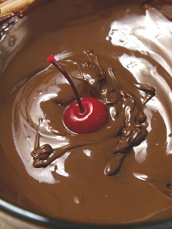 a cherry being dipped in a glass bowl of melted chocolate