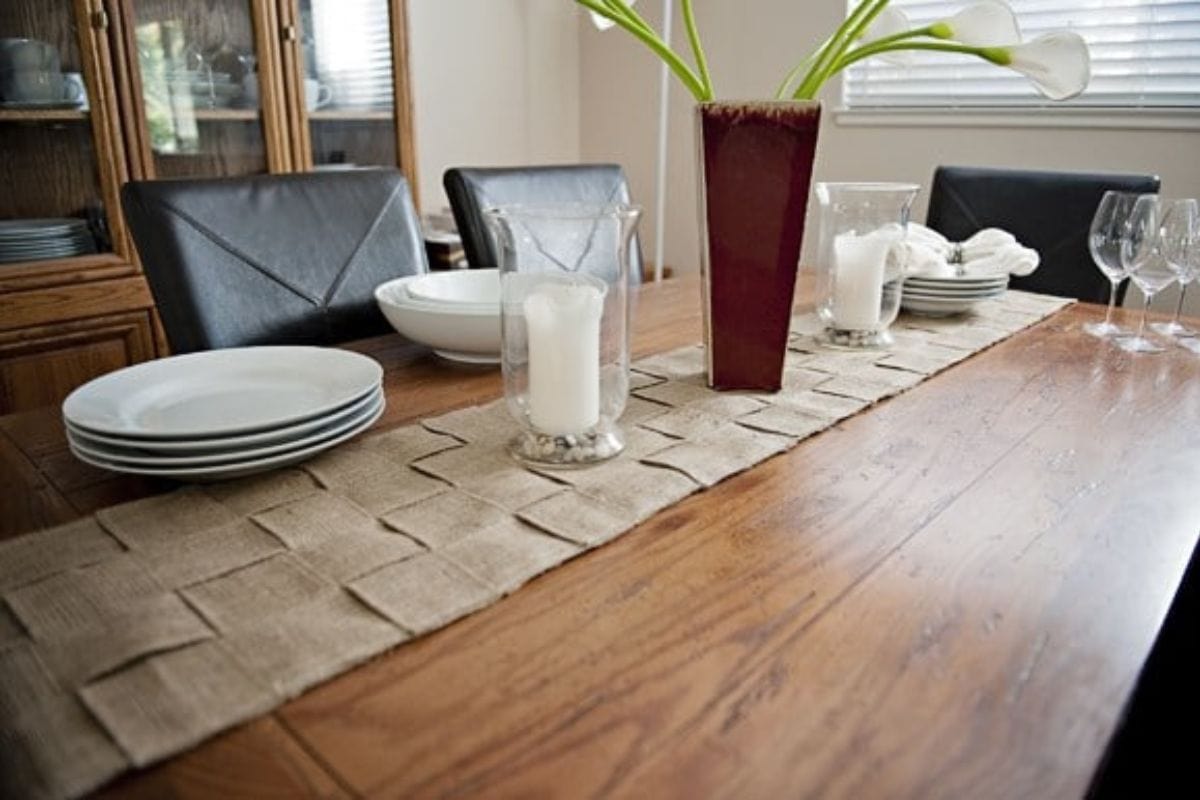 A wooden dining table with a woven beige table runner-perfect inspiration for diy burlap projects.