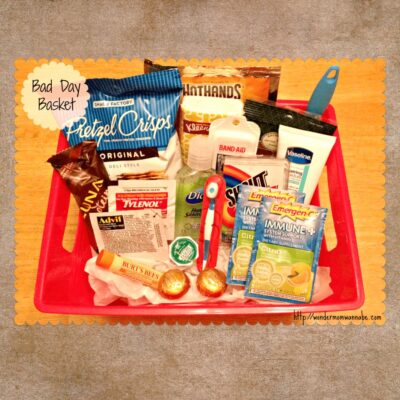 Red basket containing snacks, medications, tissues, lip balm, hand cream, bandages, mints, and personal care items—a thoughtful bad day basket labeled "Bad Day Basket" sits on a wooden surface.