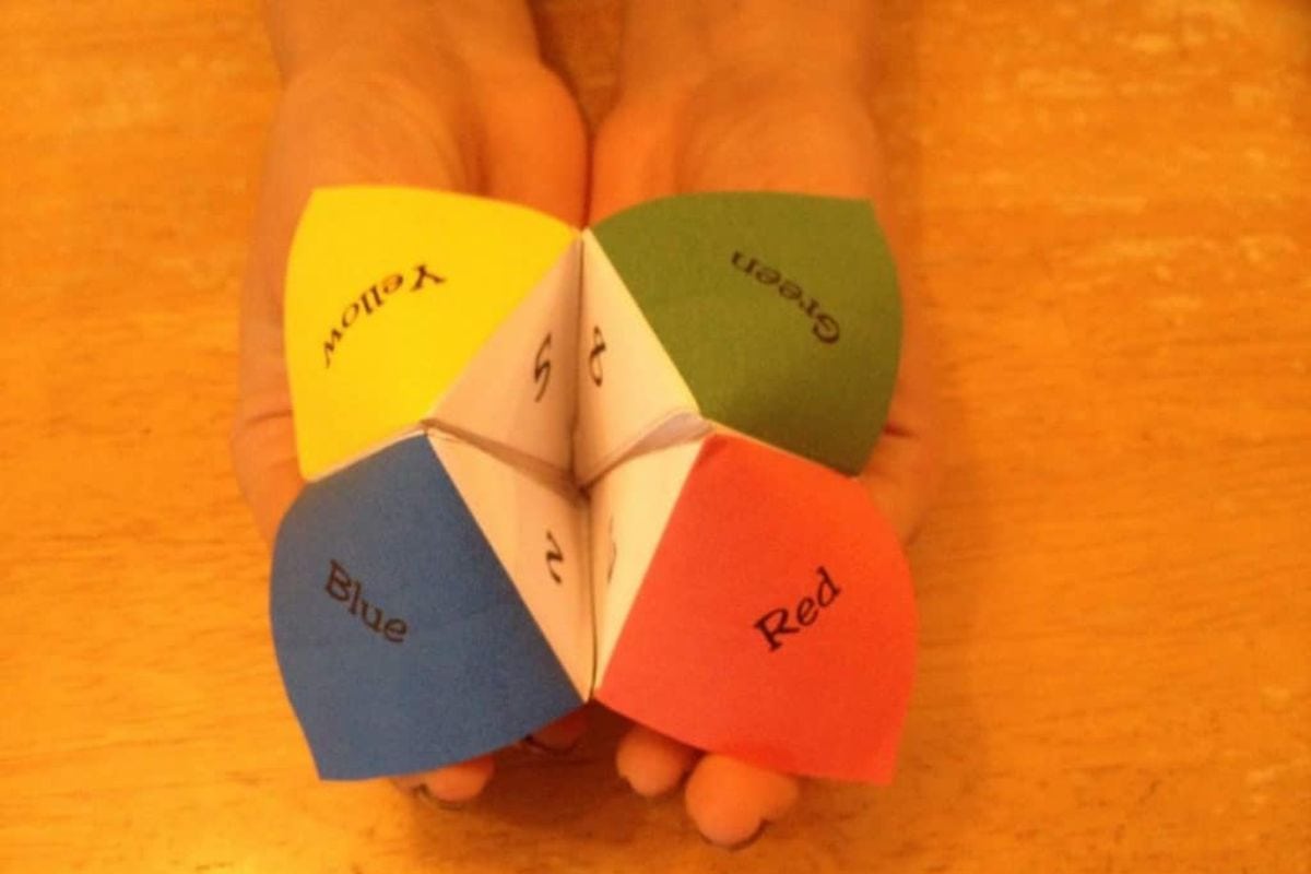 A person is holding a printable fortune teller with flaps labeled yellow, green, blue, and red, along with numbers.
