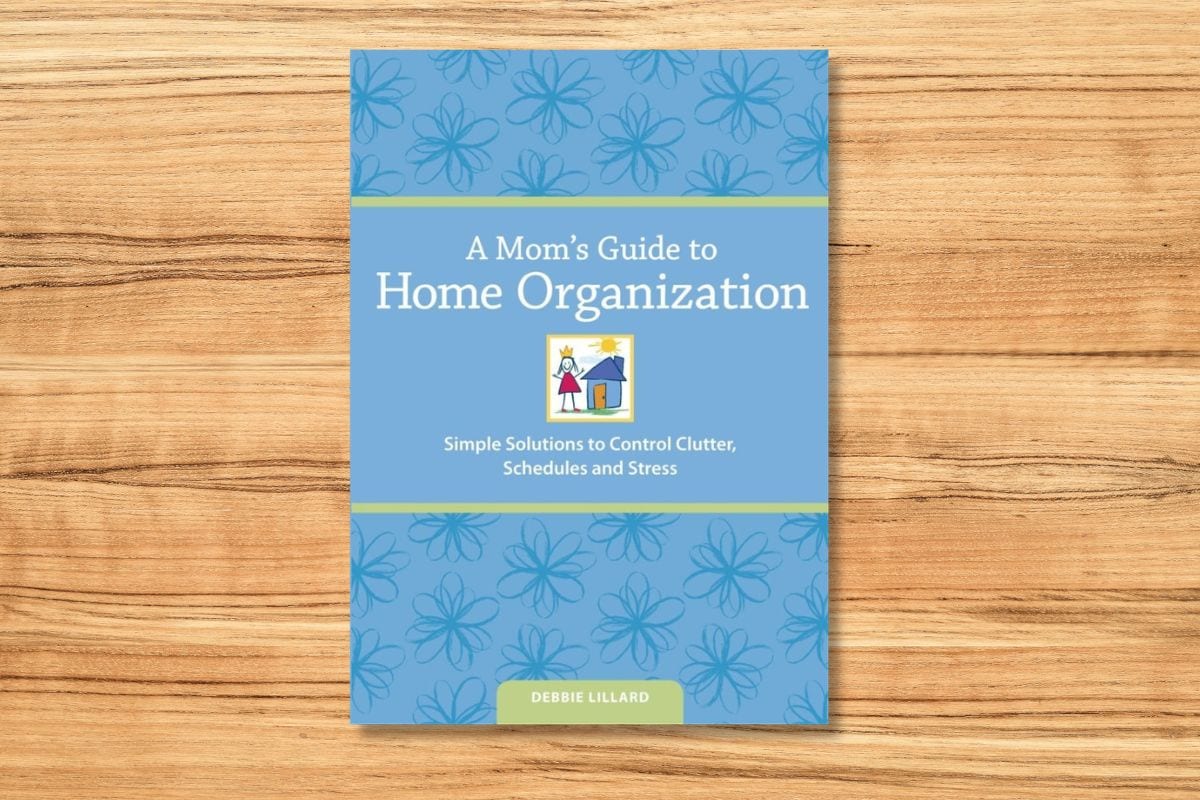 The book "A Mom's Guide to Home Organization" by Debbie Lillard rests on a wooden surface.