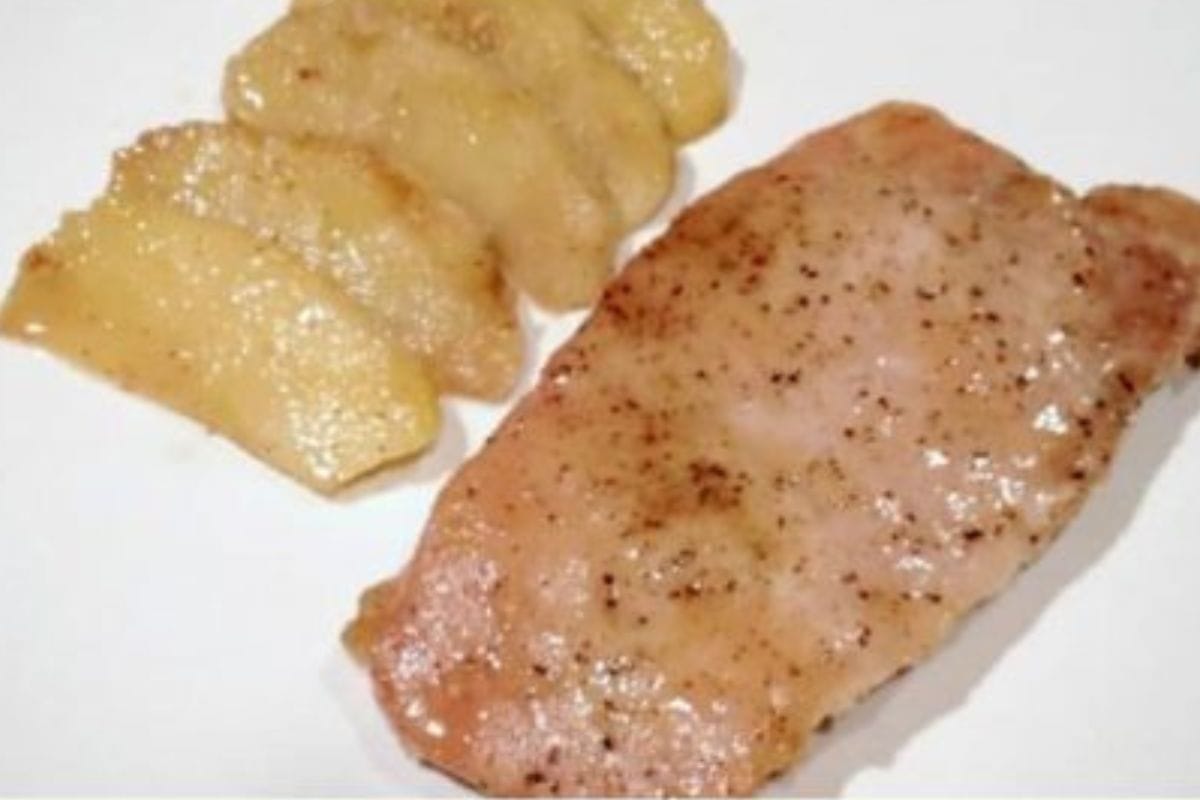A plate featuring baked pork chops and apples: a tender, pepper-seasoned pork chop paired with five slices of cooked apples, all served on a white plate.