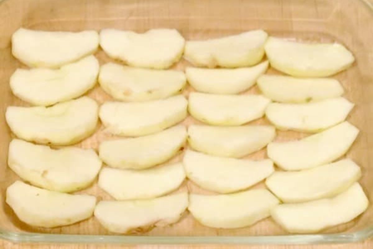 Sliced, peeled apple wedges arranged in rows on the bottom of a clear glass baking dish.