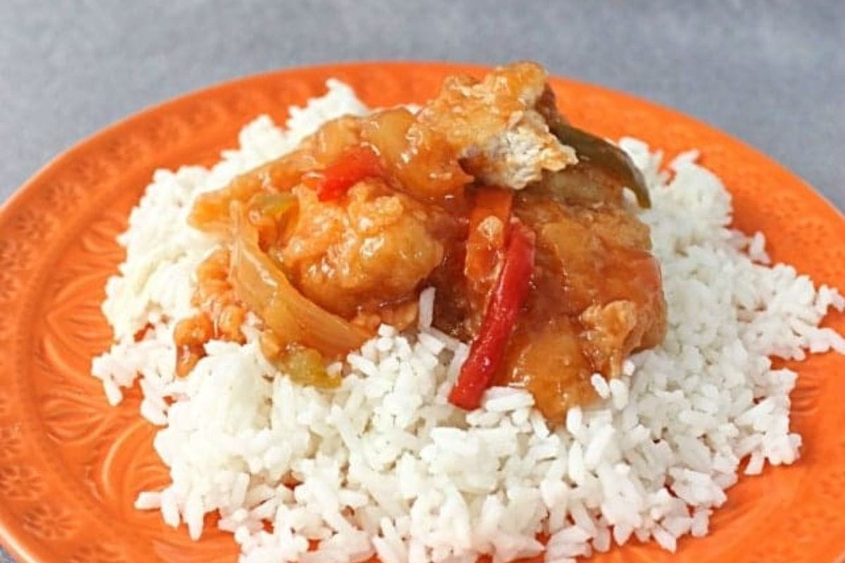 White rice topped with sweet and sour chicken, bell peppers, and onions on an orange plate-perfect for those seeking festive Chinese New Year recipes.