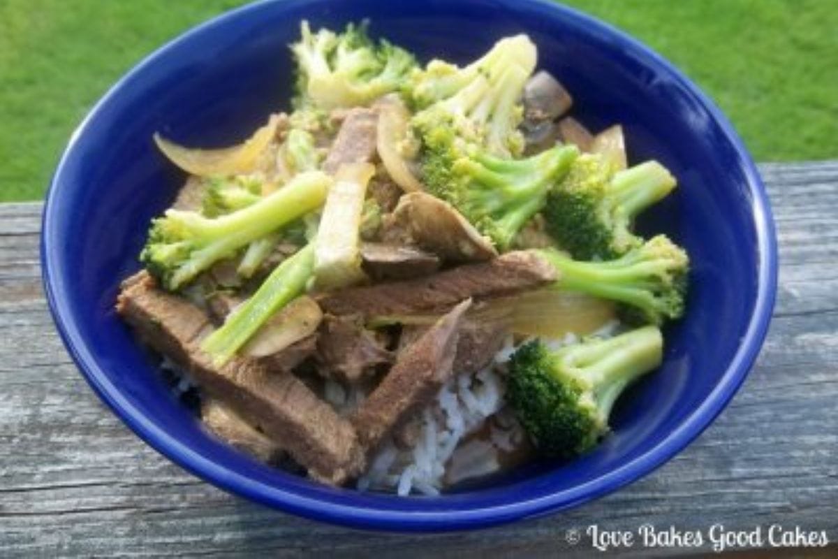 A blue bowl filled with sliced beef, broccoli florets, onions, and mushrooms served over white rice-an inviting dish for outdoor dining and a delicious choice for Chinese New Year recipes.