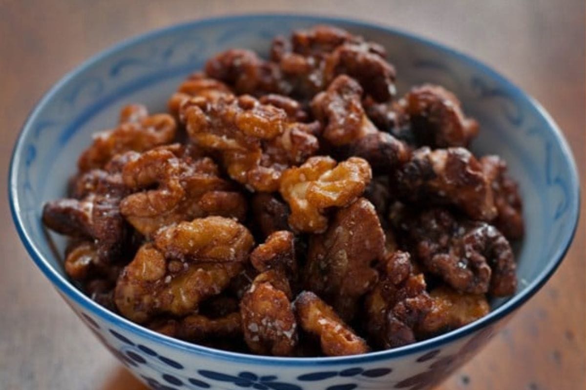 A blue and white bowl filled with glazed, roasted walnuts-perfect for Chinese New Year recipes-sits on a wooden surface.