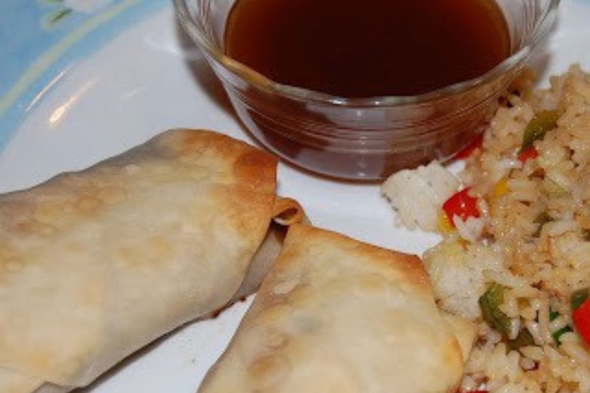 Two baked egg rolls on a plate with fried rice and a small bowl of brown dipping sauce-a tasty addition to your collection of Chinese New Year recipes.