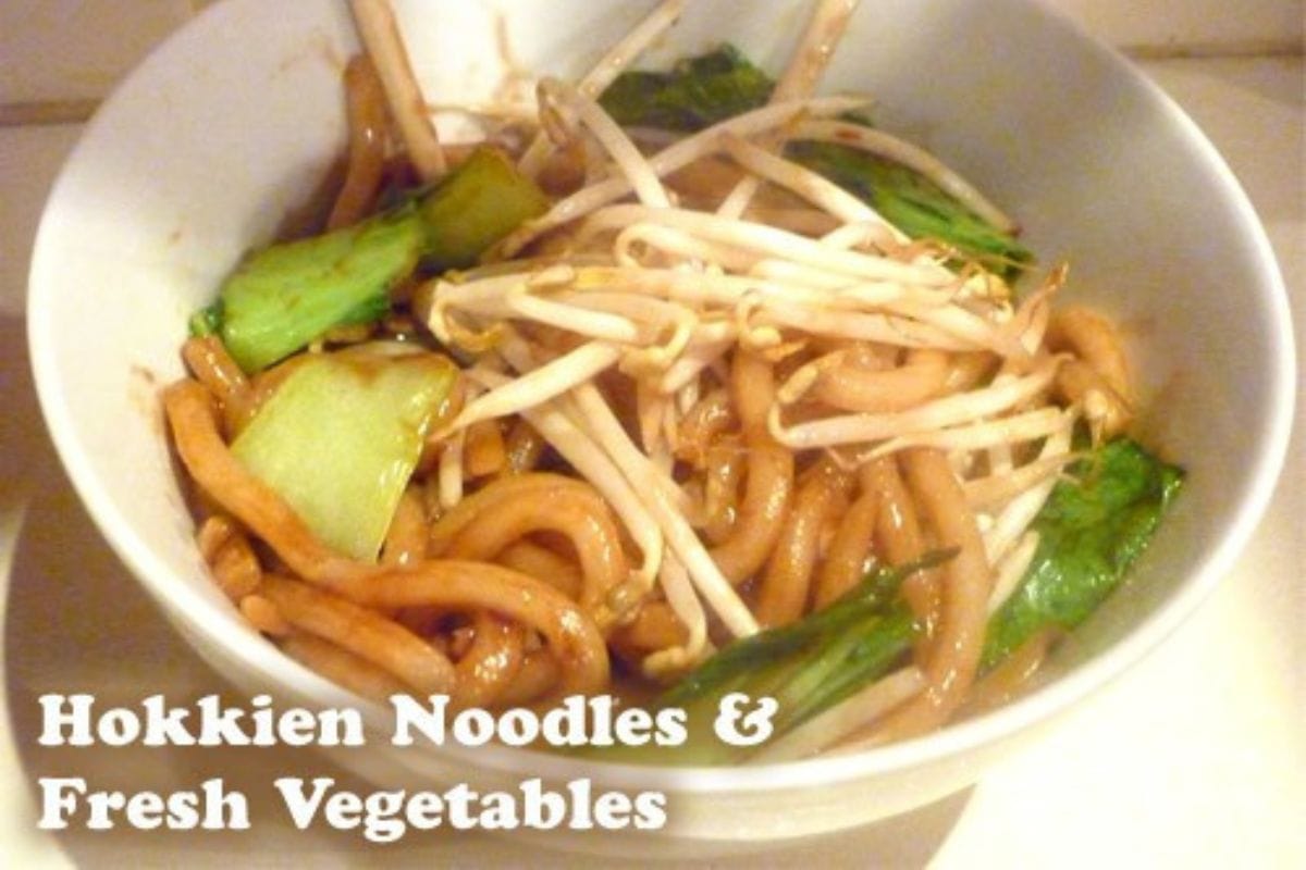 A bowl of Hokkien noodles with fresh vegetables, including bok choy and bean sprouts, perfect for chinese new year recipes. Text reading "Hokkien Noodles & Fresh Vegetables" appears in the lower left corner.