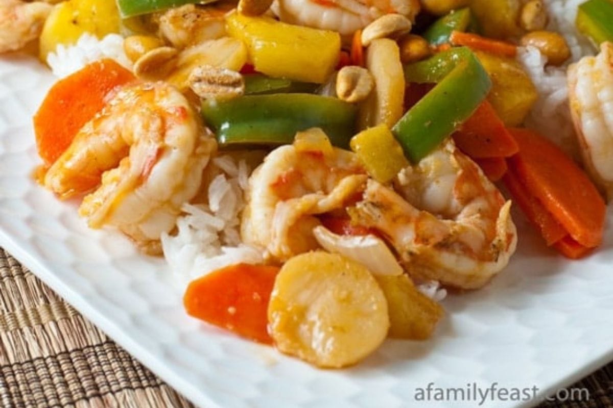 A plate of white rice topped with shrimp, carrots, green bell peppers, pineapple chunks, water chestnuts, and peanuts-a colorful dish perfect for celebrating with Chinese New Year recipes.