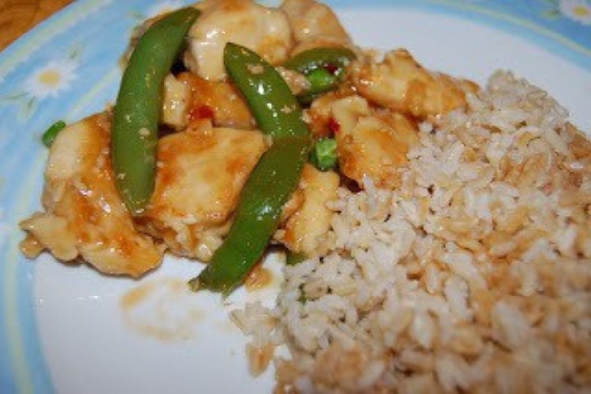 A plate with stir-fried chicken, snap peas in sauce, and a serving of brown rice-perfect for those seeking delicious Chinese New Year recipes.