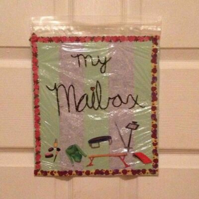 A decorated plastic bag labeled "my Mailbox" with images of mail-related items is taped to a door, offering a fun twist on family mailboxes for organizing personal notes or messages.
